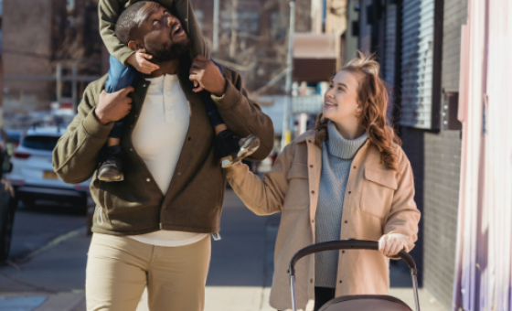 Trois personnes se promenant en ville, elles sourient. L'une porte un enfant sur ses épaules et l'autre pousse une poussette