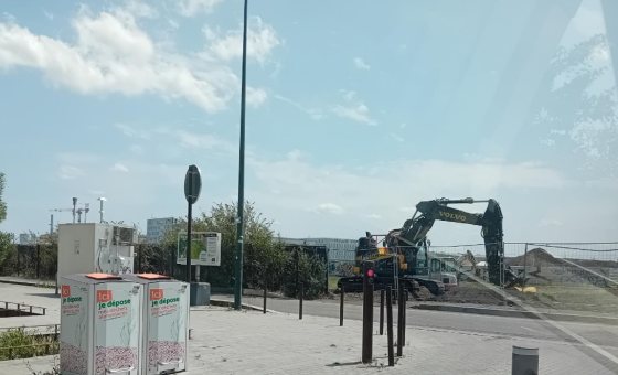 Vue de la station de mesure de la qualité de l’air située Prairie-au-Duc à Nantes, en bordure de trottoir, à proximité de deux bornes de tri alimentaire. À l’arrière-plan, un chantier est en cours avec une pelleteuse en activité.